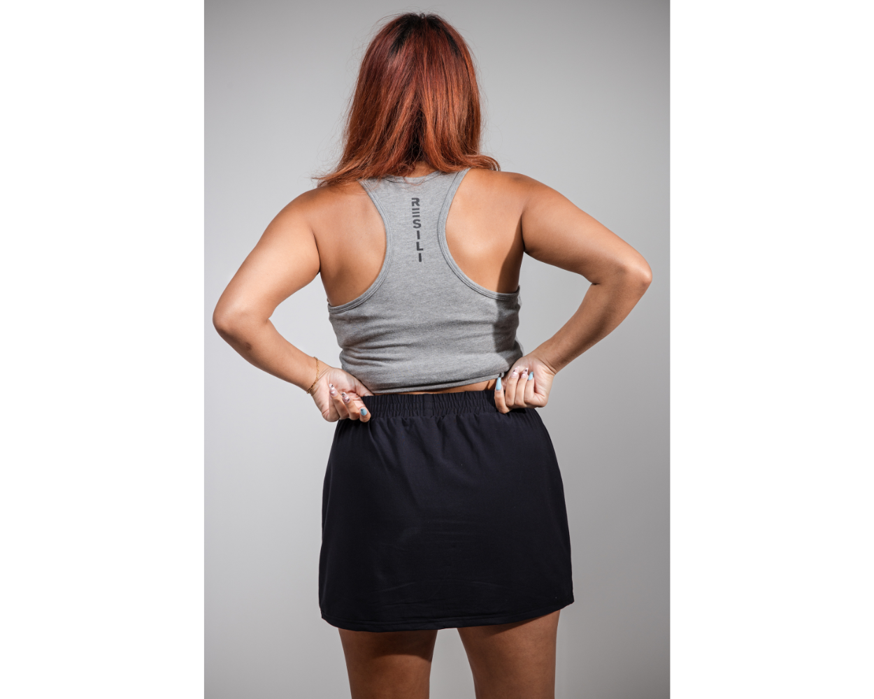 Person wearing a gray tank top and black skirt on a gray background