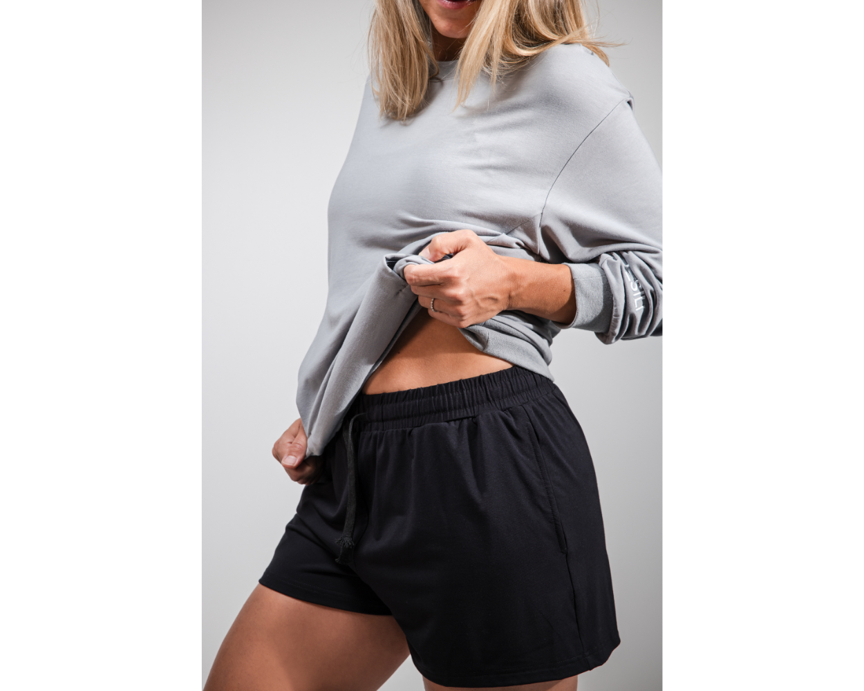 Person wearing a gray sweatshirt and black shorts on a plain background
