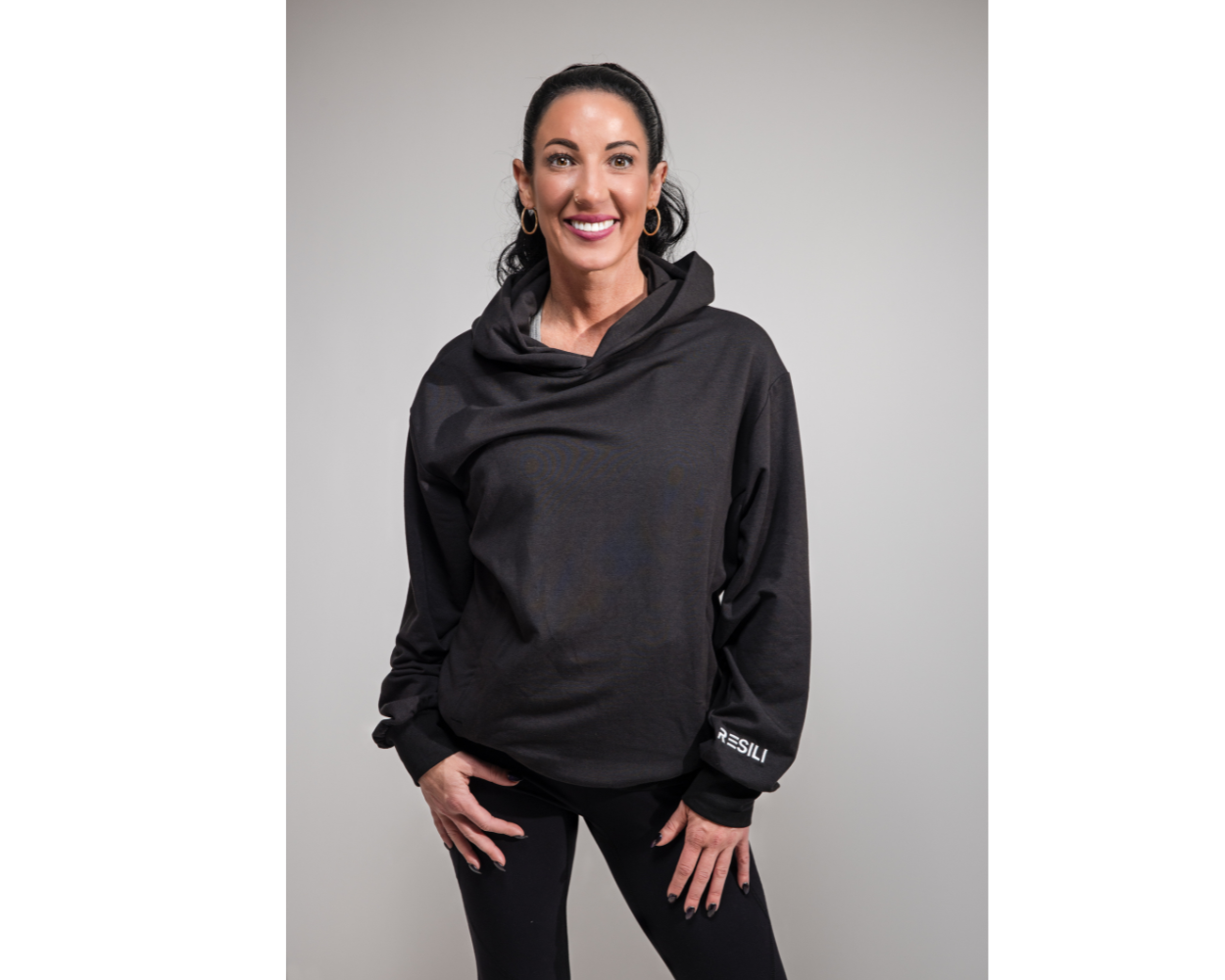 Woman wearing a black hoodie with a brand logo on a gray background