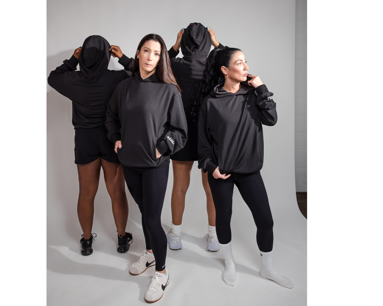 Fourwomen wearing black hoodies and pants on a gray background