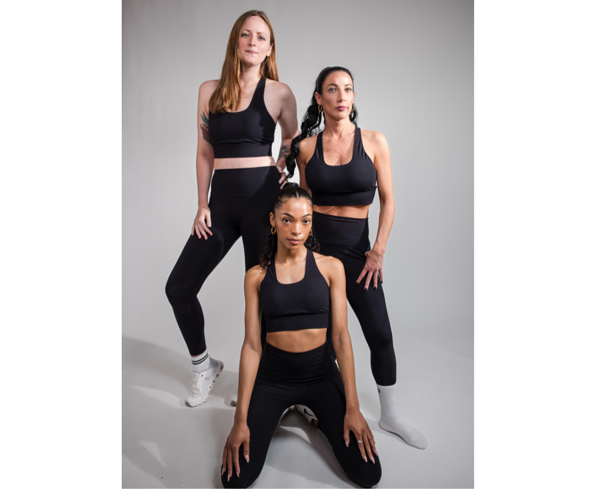 Three women wearing black athletic wear posing against a gray background
