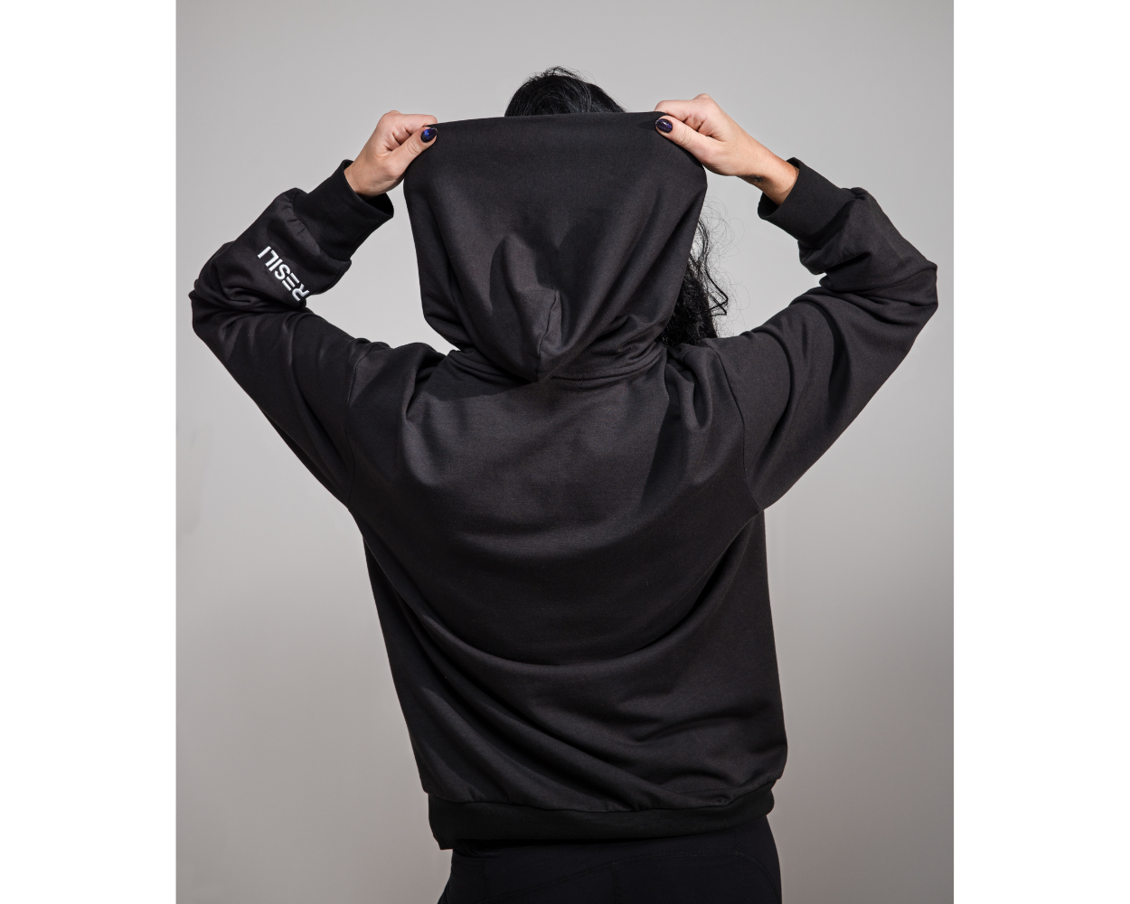 Person wearing a black hoodie with a brand logo on a gray background