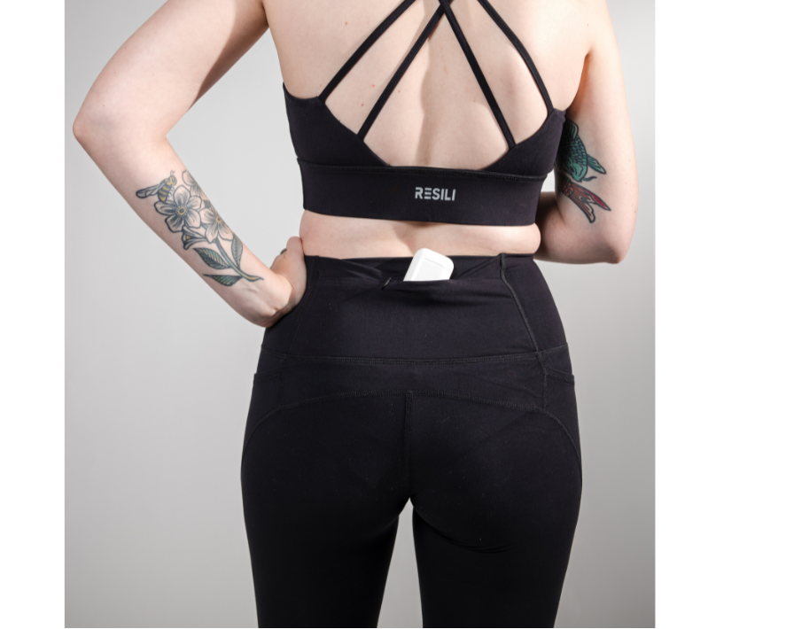 Person wearing a black sports bra and leggings with a visible brand logo on a gray background
