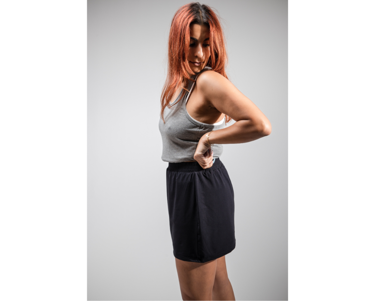 Woman in gray tank top and black skirt posing against a gray background