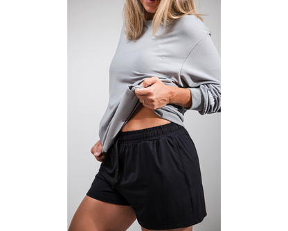 Person wearing a gray sweatshirt and black shorts on a plain background