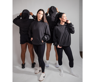 Fourwomen wearing black hoodies and pants on a gray background