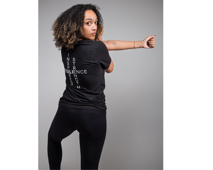 Person wearing a black t-shirt with text, standing against a gray background