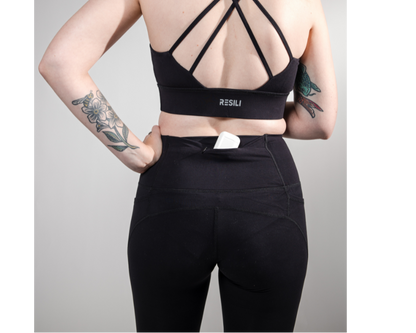 Person wearing a black sports bra and leggings with a visible brand logo on a gray background